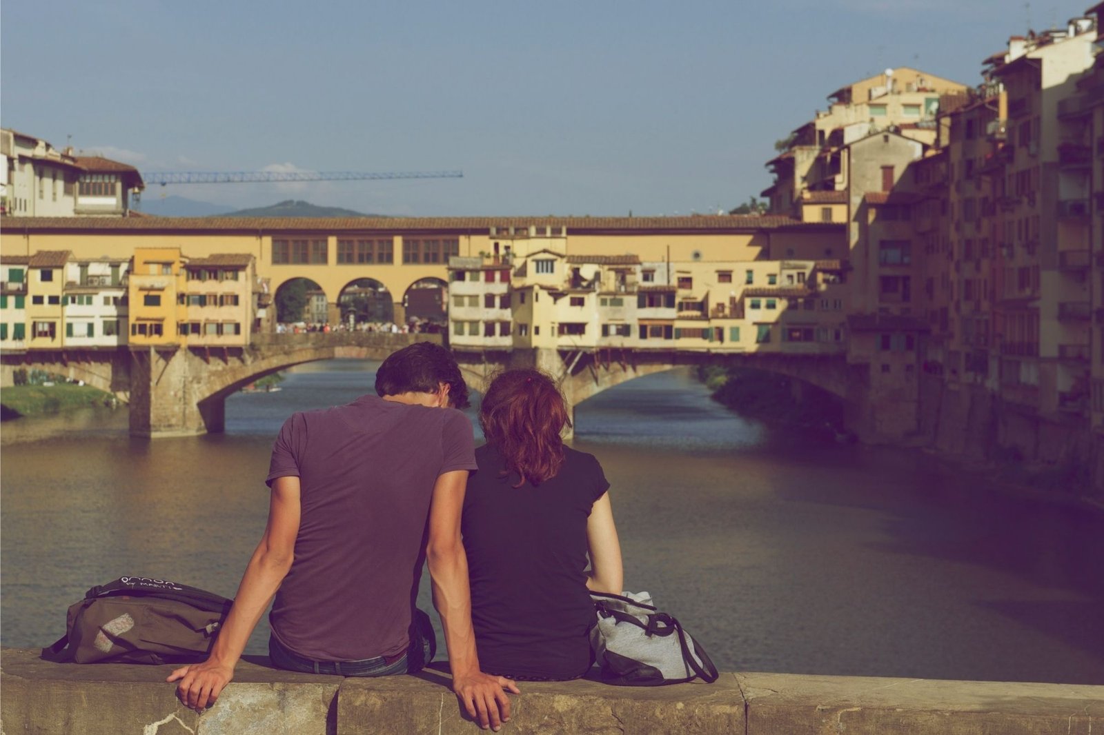 Pärchen sitzt auf Brücke mit Blick auf Ponte Vecchio in Florenz