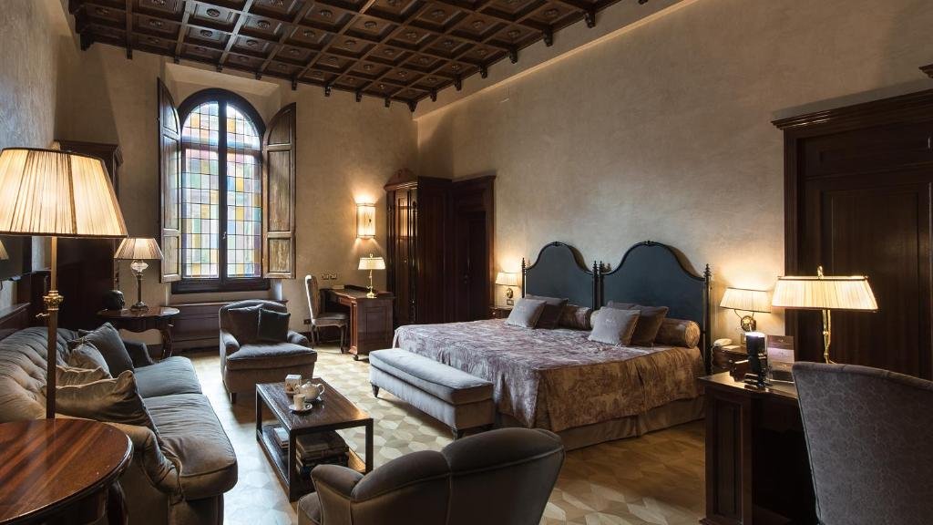 Zimmer mit Fenster aus Buntglas und dunklen Holzelementen im Hotel Baglioni in Florenz