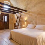 Helles Zimmer mit Balken und Steinwänden mit weißem Doppelbett in Matera
