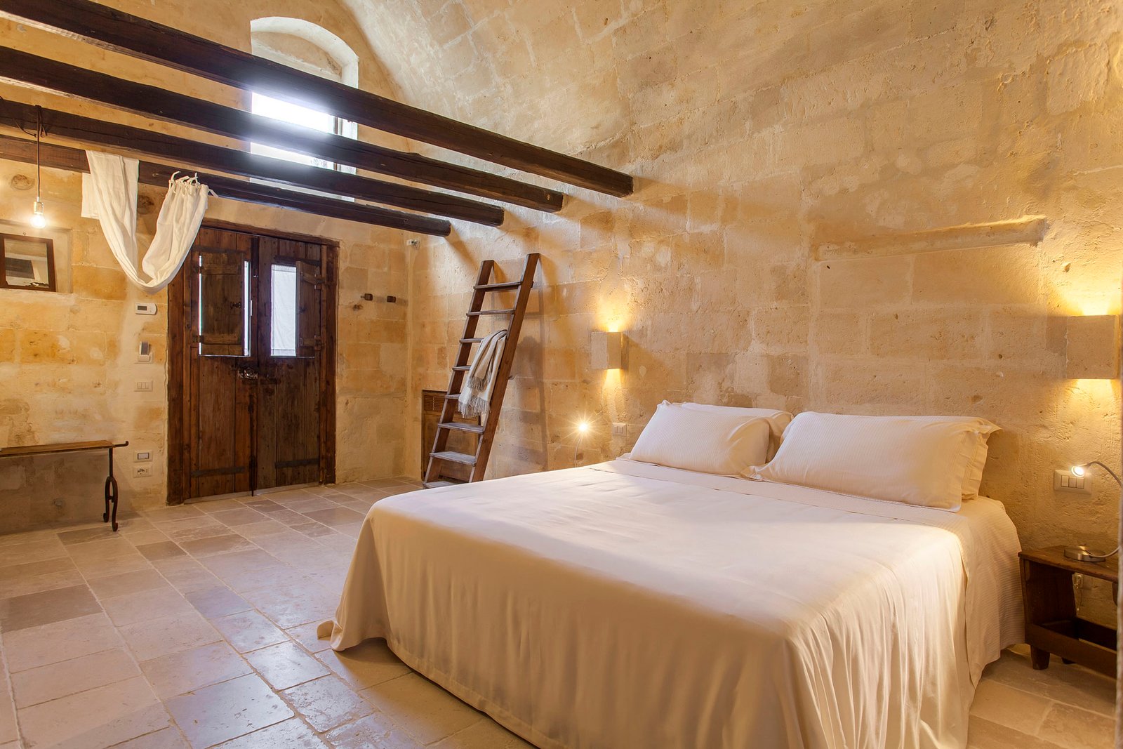 Helles Zimmer mit Balken und Steinwänden mit weißem Doppelbett in Matera
