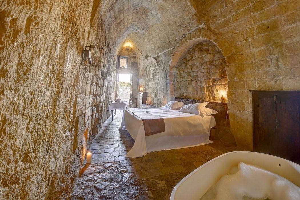 Hotelzimmer in Höhle in Matera mit hellen steinernen Wänden und weißem Doppelbett