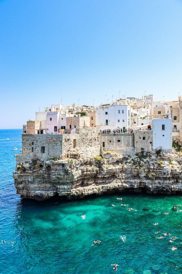 Blick auf Klippe von Polignano a Mare in Apulien mit badenden Menschen und weißen Häusern auf Klippe