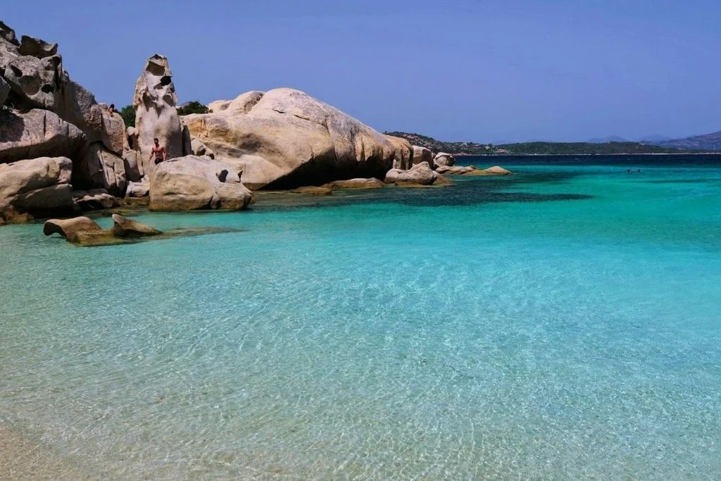 Strand mit türkis-transparentem Wasser und runden Felsen