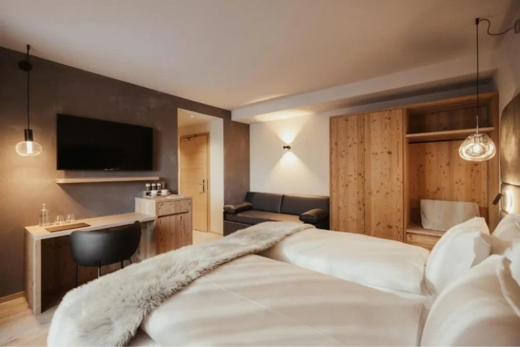 Hotelzimmer mit Holzakzenten und Doppelbett mit weißem Bezug und Fell am Fußende